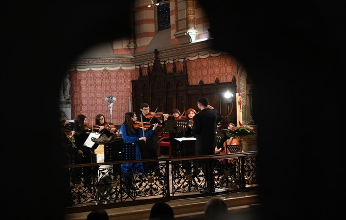 Slika prikazuje grupu mladih muzičara koji nastupaju u unutrašnjosti bogato ukrašene crkve. 