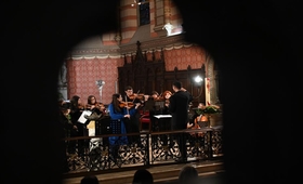 A small ensemble of musicians is performing inside a richly decorated venue that appears to be a historical churc