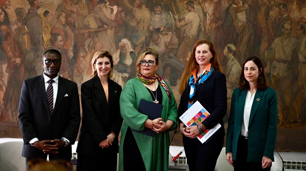  Four women and man posing standing in front of a captivating painting.