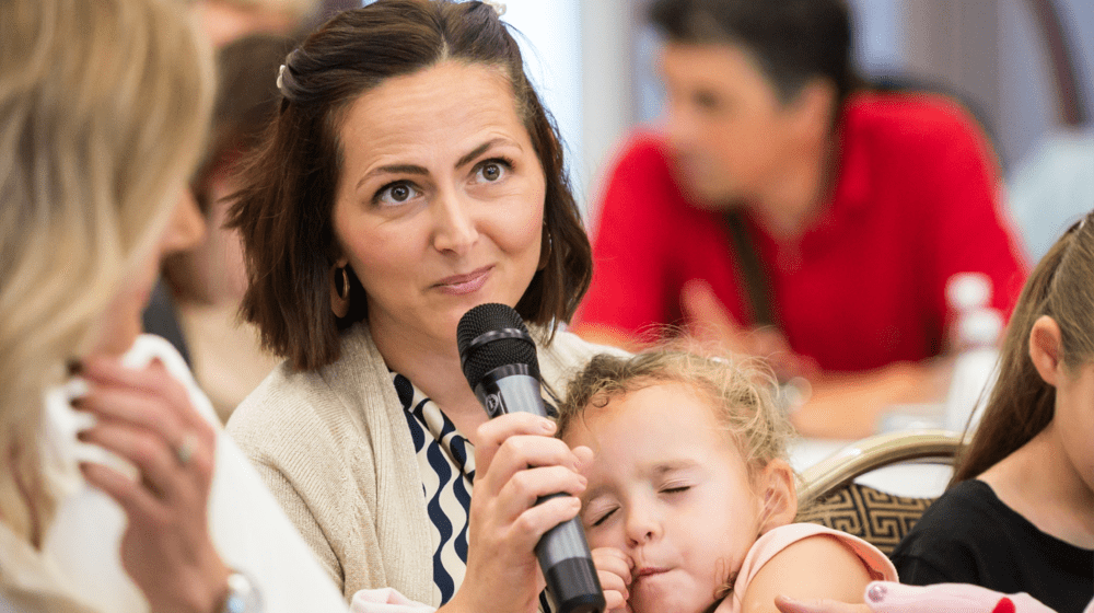 A woman speaking into a microphone while holding her child 