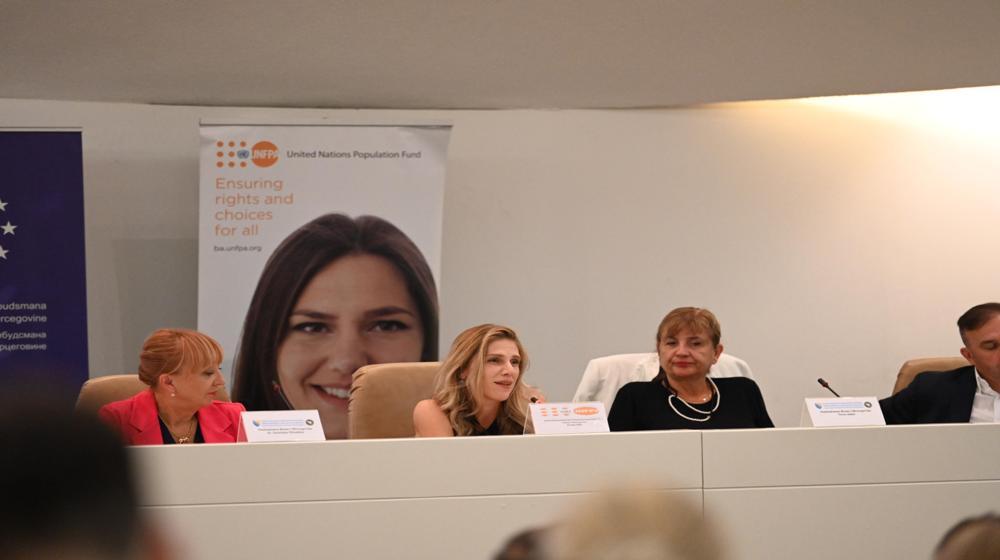 The panelists, three women and one man, are engaged in discussion. The central banner features a close-up image of a smiling woman, symbolizing the focus on women's rights and health.